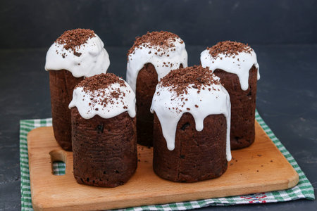 Easter cakes baked for Easter and coated with sugar icing are located on a wooden board against a...