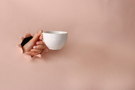 White cup in a female hand through round hole in pink paper, Coffee time, Copy space
