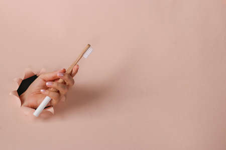 Wooden toothbrush in a female hand through round hole in pink paper, Zero waste conceptの写真素材