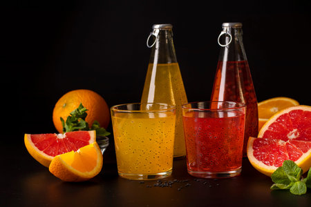 Trendy tropical orange and grapefruit juice with basil seeds in bottle on black background, Closeup