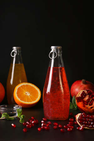 Trendy pomegranate and orange drink with basil seeds in bottles on black background, Closeup, Vertical formatの写真素材