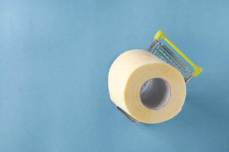 Grocery trolley with roll of soft toilet paper on blue background, Deficit, Increased unexpected...