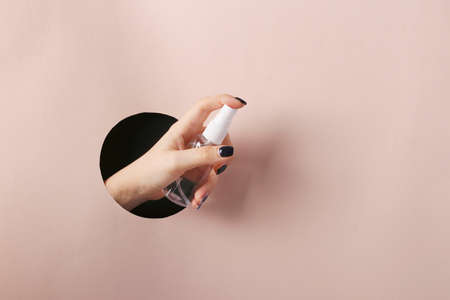 Female hand holds antiseptic for hands through a round hole in pink paper, Covid-19 pandemic, copy spaceの写真素材