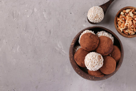 Energy balls of nuts and oatmeals with coconut flakes and cocoa in coconut bowl on gray background,...