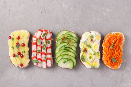 Five sandwiches on toast with fresh carrots, cucumbers, pineapple, red currant, crab sticks and...