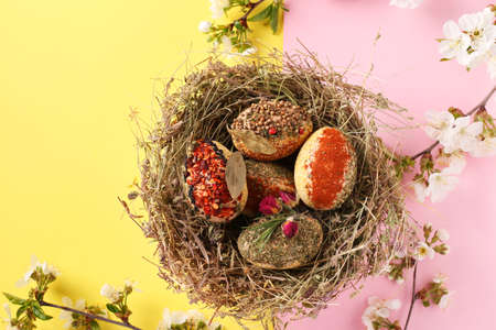 Easter eggs in a nest of herbs, decorated with various spices and cereal without dyes and preservatives on a pink and yellow background, Top viewの写真素材