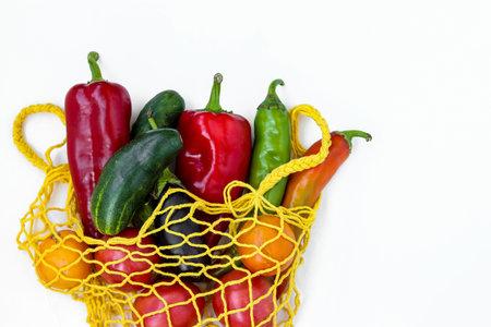 Fresh organic vegetables in a yellow shopping mesh bag on white background, horizontal format, Zero...