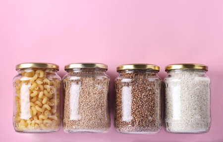 Storage of rice, buckwheat, wheat groats and pasta in glass jars. Crisis food stock for quarantine isolation period on pink background, Zero waste concept, Space for textの写真素材