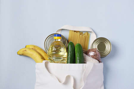 Food delivery, Donation. Textile Bag with food supplies crisis food stock for quarantine isolation period on blue background. Rice, buckwheat, pasta, canned food, cucumbers, bananas, vegetable oilの写真素材