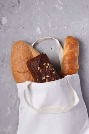 Handmade reusable cotton textile shopping bag with fresh bread on a gray concrete background. Zero...