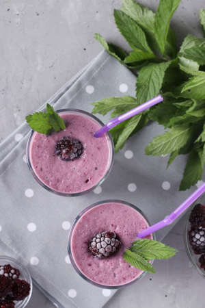 Two servings of homemade smoothies with frozen blackberries in glasses on gray concrete background, Diet and weight loss control concept, Vertical formatの写真素材