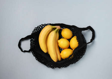 Yellow ripe bananas and lemons in black string mesh bag on light background, Zero waste concept, Top viewの写真素材