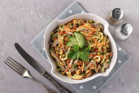 Salad with chicken hearts, cucumber, carrots, onions and peas in a white bowl on a gray concrete background, Horizontal format, Top viewの写真素材