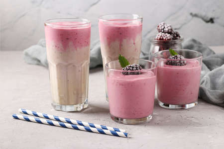 Four servings of homemade protein cocktail with frozen blackberries, bananaand yogurt in glasses on gray concrete background, Diet and weight loss control conceptの写真素材