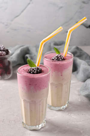 Two servings of protein cocktail with frozen blackberries, banana and yogurt in glasses on gray concrete background, Diet and weight loss control concept, Vertical formatの写真素材