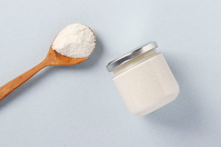 Vegan organic paste of coconut in glass jar and coconut flour in spoon on light blue background,...