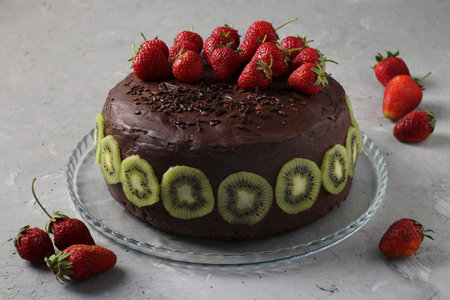 Chocolate homemade cake decorated strawberries and kiwi located on gray concrete background,...