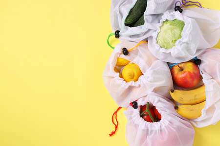 Fruits and vegetables in reusable eco friendly mesh bags on bright yellow background. Space for text, Zero waste concept, Stop pollution.の写真素材