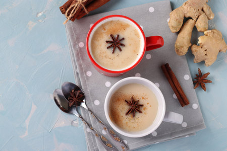 Traditional indian masala tea with spices in two cups on light blue background, horizontal format, Top view