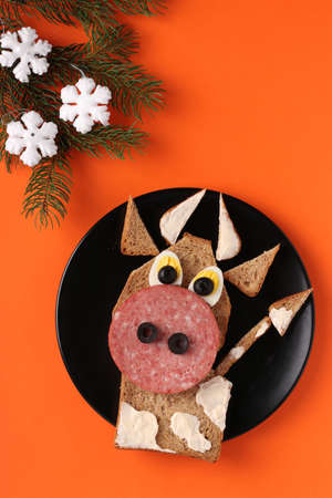 Sandwich with sausage and egg in the shape of a funny bull, symbol of the new 2021 on bright orange background, culinary idea for children, Vertical formatの写真素材