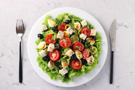 Healthy salad of cherry tomatoes, cucumbers, peppers, black olives, with olive oil, quail eggs and gorgonzolla cheese on a light background, top viewの写真素材