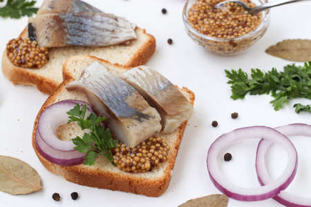 Snack from salted herring on bread with red onion and mustard on white background, Closeupの写真素材