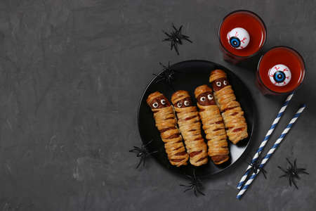 Spooky sausage mummies and tomato juice for Halloween party on dark plate, Top view. Flat lay. Space for text.の写真素材