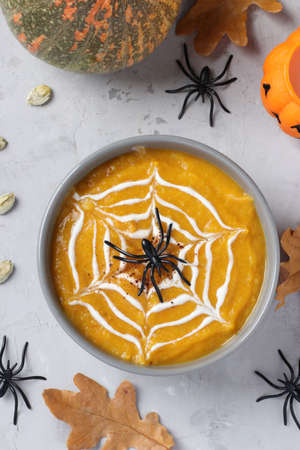 Halloween pumpkin soup with creamy spider web in gray bowl and spiders on the table. Vertical format.の写真素材