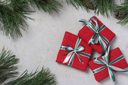 Three Christmas gifts in red paper with green and white ribbons on gray background. Xmas holiday...