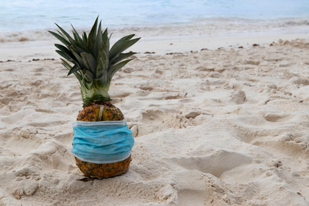 Pina colada drink in pineapple in protective face mask on the sand on the coast Caribbean Sea. Vacation and travel concept during quarantine.の写真素材