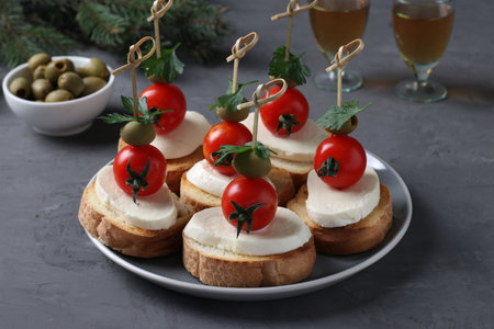 Canapes of mozzarella, cherry tomatoes, green olives, parsley on croutons of white bread on dark gray background. Festive New Year snack. Closeupの写真素材