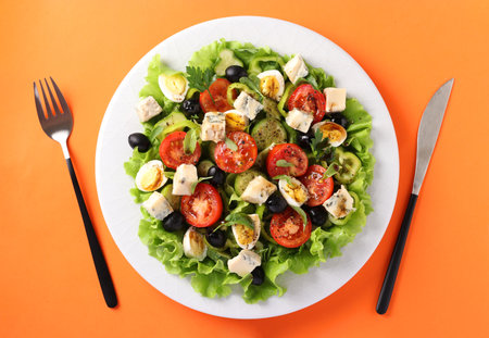 Healthy salad of cherry tomatoes, cucumbers, peppers, black olives, with olive oil, quail eggs and gorgonzolla cheese on a orange background. View from aboveの写真素材