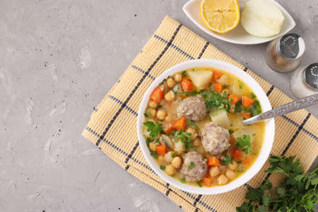 Turkish soup with chickpeas, meatballs and vegetables in a white bowl on a gray background. With place for text. Top viewの写真素材