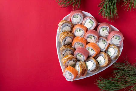 Asian food with sushi set of salmon, tuna and eel with philadelphia cheese on plate in the shape of a heart against a red background. View from above. Space for textの写真素材