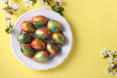 Marble eggs painted with food colors for Easter localed on a white plate on yellow background. Top...