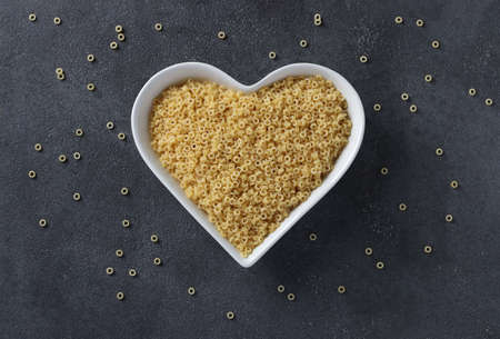 Raw pasta ditalini on heart-shaped plate on dark gray table. View from aboveの写真素材