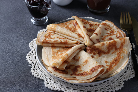 Lush homemade pancakes with wheat flour, eggs and yogurt, served with berries jam on gray background