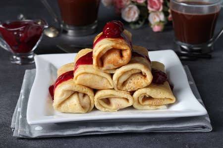 Homemade pancakes with curd filling and cherry sauce on a white plate on a dark background.の写真素材
