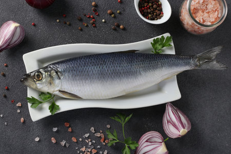 Salted herring with red onion, peppers, sea salt and parsley on gray background. View from above