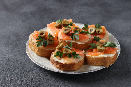 Canapes of salted salmon, green olives and parsley on croutons of white bread on dark background....