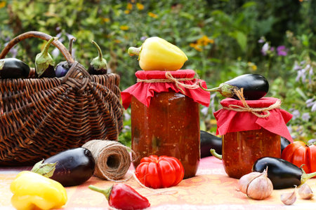 Homemade adzhika and eggplants in tomatoes sause in jars located on a table in the garden. Harvesting for the winter. Horizontal format.の写真素材