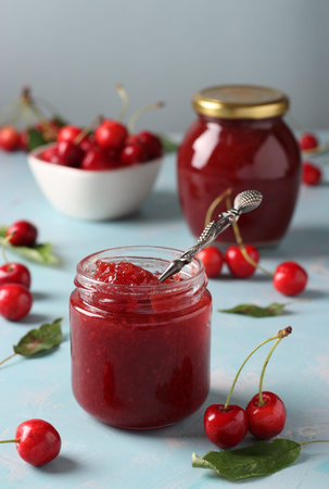Two jars of homemade jam of sweet cherry on a light blue background