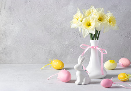 Still life with daffodils in a vase, Easter bunny and colorful eggs on a light background. Festive...