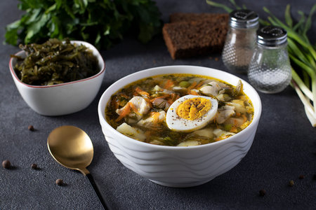 Kelp and chicken soup served with boiled egg in a white bowl on dark background. Close-up