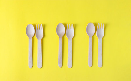 Wooden forks and spoons, eco friendly disposable kitchenware utensils on yellow background. Zero...