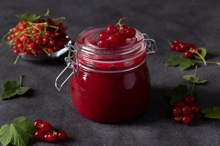 Glass jar of homemade red currant jam on a dark background. Close-up. Horizontal format
