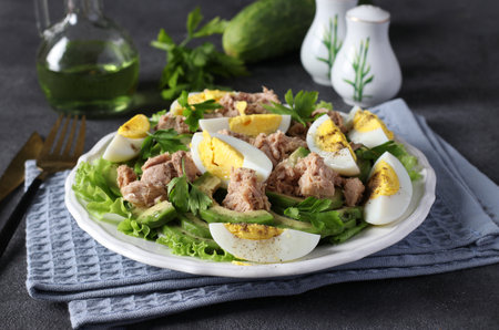 Healthy salad with avocado, tuna, eggs and cucumbers on a white plate on a dark gray background. Close-upの写真素材