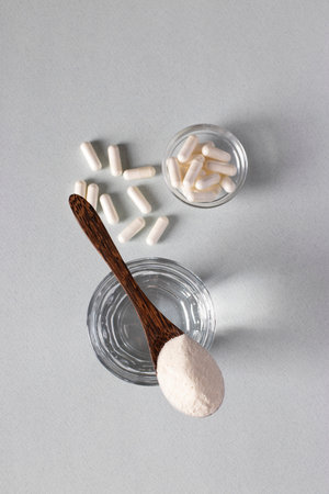 Collagen powder in spoon on glass of water, collagen capsules on light background, healthy and...
