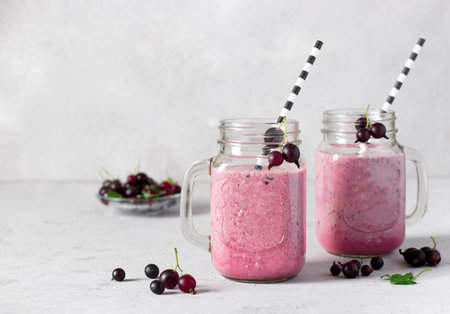 Smoothie with natural yogurt and black currant with drinking straw in glass jars on light gray...