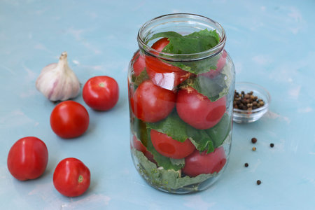 The process of preparing pickled tomatoes with grape leaves and garlic. Location on a light blue...